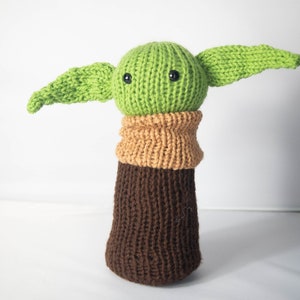 K&ouml;nnte beinhalten: Ein gr&uuml;nes, gestricktes Pl&uuml;schtier mit gro&szlig;en Ohren und braunen, gestrickten Beinen. Das Spielzeug hat schwarze Knopfaugen und einen gestrickten braunen Kragen.