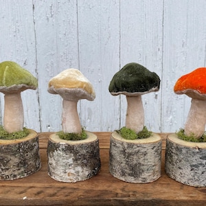 May include: Four velvet mushroom figurines with different colored tops, displayed on wooden bases. The mushrooms are green, cream, dark green, and orange.