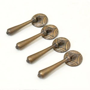 以下が含まれることがあります： 装飾的な円形のデザインが施されたアンティークブラスのキャビネットプル4個。各プルには、長く細いハンドルが付いています。