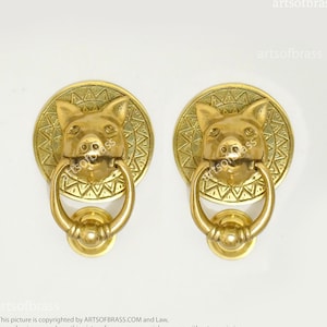 May include: Two gold-toned door knockers with pig head designs. Each knocker has a round, ornate base with a ring handle.