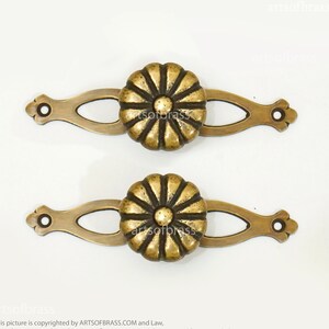 Puede incluir: Dos tiradores de cajón de latón con un diseño floral decorativo. Cada tirador tiene una base ovalada larga con un pomo floral decorativo.