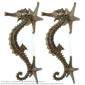 Könnte beinhalten: Zwei bronzene Türgriffe in Form von Seepferdchen mit Seeestern-Details. Die Seepferdchen sind in 'S'-Form gekrümmt und haben eine strukturierte Oberfläche.