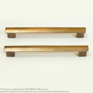 May include: Two brushed brass cabinet pulls with a rectangular shape and rounded edges. The pulls are arranged horizontally, one above the other.