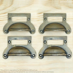 May include: Four antique brass drawer pulls with a rectangular label holder. Each pull has a rounded, slightly domed shape and is accented with small, round rivets.