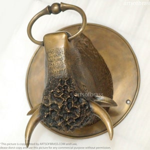 May include: A bronze bull's head wall mount with a ring handle. The bull's head is detailed with textured horns and a textured face. The bull's head is mounted on a round bronze plate.