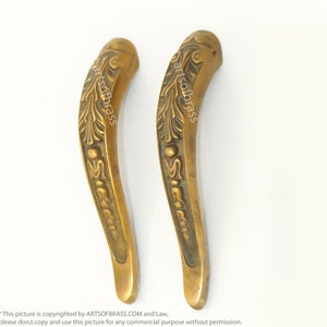 May include: Two ornate brass door handles with a floral design. The handles are curved and have a decorative knob at the top.