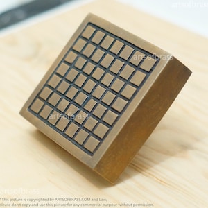May include: A square brass door handle with a grid pattern. The handle is made of solid brass and has a polished finish.