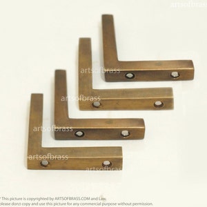 May include: Four brass corner brackets, each with four holes. The brackets are stacked on top of each other, with the largest bracket at the bottom and the smallest bracket at the top.