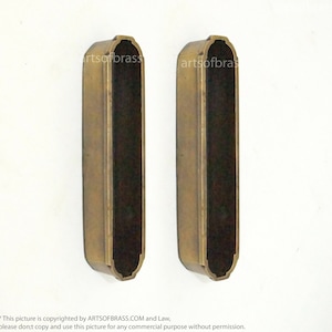 May include: Two brass door pulls with a black insert. The pulls have a decorative design around the edges.