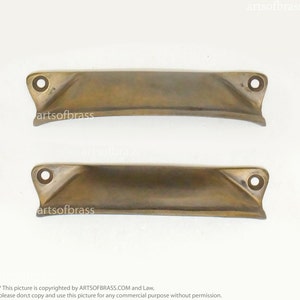 May include: Two antique brass cabinet door pulls with rounded edges and a subtle curve. Each pull has a single hole for mounting.