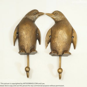 Peut inclure: Deux crochets en forme de pingouin dorés avec une finition texturée. Les crochets sont face à face et ont une extrémité arrondie en forme de boule.