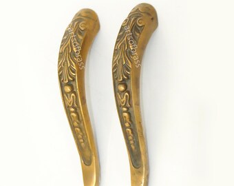 May include: Two ornate brass door handles with a floral design. The handles are curved and have a decorative knob at the top.