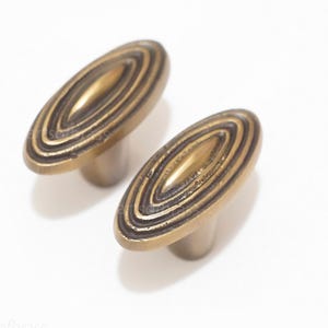 Peut inclure: Deux boutons de cabinet ovales en laiton avec un motif de cercles concentriques. Les boutons ont une finition brossée et sont de couleur or chaud.