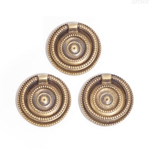 May include: Three antique brass cabinet knobs with a ring pull and decorative concentric circles.