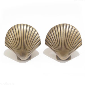 Może przedstawiać: Dwa mosiężne uchwyty do szuflad w kształcie muszli z żebrowanym wzorem.