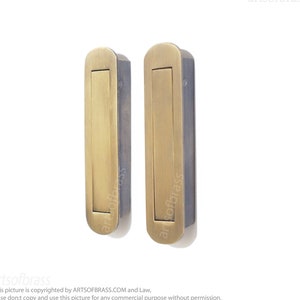 Könnte beinhalten: Zwei Messing-Schranktürgriffe mit rechteckigem Einsatz und abgerundeten Kanten. Die Griffe sind auf einem weißen Hintergrund montiert.