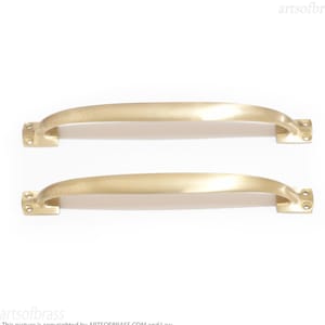 May include: Two gold-toned cabinet door pulls with a simple, curved design. The pulls are made of solid brass and have a satin finish.