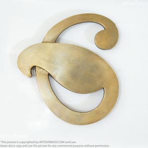 Könnte beinhalten: Ein goldfarbener Metallbuchstabe S mit einem einzigartigen, stilisierten Design. Der Buchstabe ist aus massivem Messing gefertigt und hat eine glatte, polierte Oberfläche.