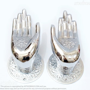 May include: A pair of polished silver door handles shaped like hands with intricate floral designs. The handles are mounted on round plates with ornate borders.