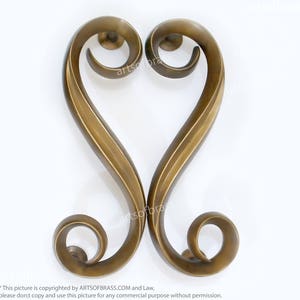 May include: A pair of ornate, gold-toned, brass door handles in the shape of a heart. The handles have a swirling, decorative design.
