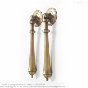 May include: Two antique brass door pulls with a long, slender, tapered design. The pulls have a round, decorative top with a raised edge.