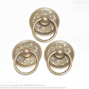 May include: Three ornate brass door pulls with intricate floral designs. Each pull features a circular ring handle and a decorative backplate.