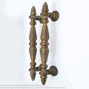 May include: A pair of ornate brass door handles with a decorative, fluted design. The handles are attached to a wall with a single screw.