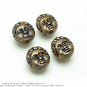 May include: Four antique gold-toned metal buttons with a raised design of a face. The buttons have a textured surface and a slightly rounded shape.