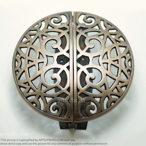 May include: A pair of round, ornate brass door handles with a decorative, intricate, cut-out design. The handles are separated by a metal bar.
