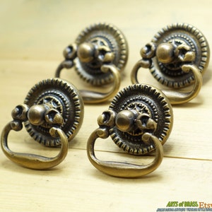 May include: Four antique brass drawer pulls with ornate designs and a ring handle. The pulls have a circular base with a raised centre knob and a decorative border.