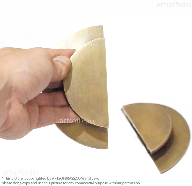 May include: Two brass door pulls in the shape of half circles, one is stacked on top of the other. The pulls are shown against a white background.