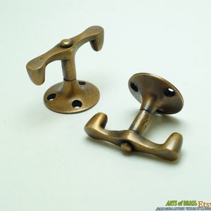 May include: Two antique brass hooks with a unique design. The hooks are mounted on a round base and have a curved shape. The hooks are perfect for hanging coats, hats, or other items.