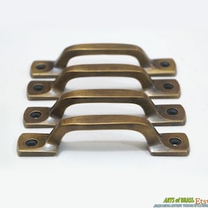 May include: Four antique brass cabinet pulls with a rounded rectangular shape and a slightly curved handle. The pulls are arranged in a row, with the top pull slightly offset from the others.