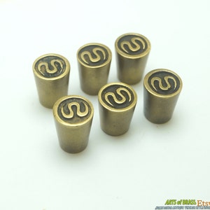 Pode incluir: Seis botões de armário de latão com um design de espiral decorativo. Os botões são de cor dourada clara e têm forma cilíndrica.