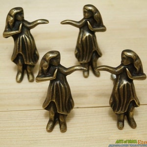 May include: Set of four antique brass cabinet knobs featuring a stylized hula dancer design. Each knob is approximately 2 inches tall and has a screw hole on the back for installation.