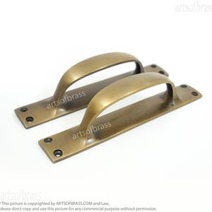 Puede incluir: Dos tiradores de puerta de latón antiguo con un diseño curvo. Los tiradores miden aproximadamente 15 cm de largo y tienen un acabado pulido.