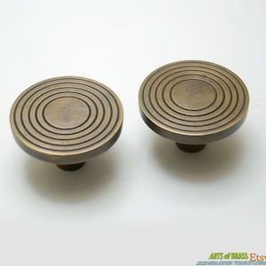 May include: Two brass cabinet knobs with a circular design featuring concentric circles. The knobs have a slightly aged, antique finish.