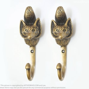 May include: Two gold-toned fox head hooks. The hooks are made of metal and have a detailed fox head design. The hooks are mounted on a white background.
