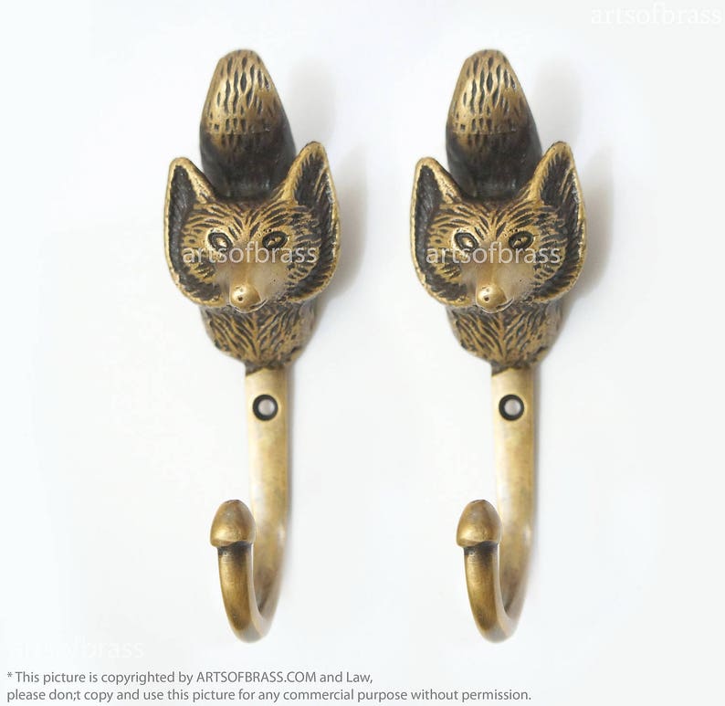 May include: Two gold-toned fox head hooks. The hooks are made of metal and have a detailed fox head design. The hooks are mounted on a white background.