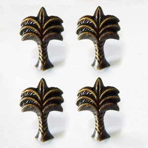 Puede incluir: Juego de cuatro pomos de armario de palmera de oro antiguo. Cada pomo presenta un diseño de palmera detallado con un tronco texturizado.