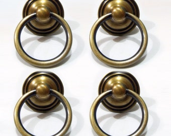 May include: Four antique gold-toned ring cabinet pulls with a black accent ring. The pulls have a round, raised center knob.