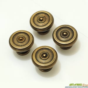 May include: Four antique brass cabinet knobs with a circular design and a raised center. The knobs have a slightly aged, tarnished finish.