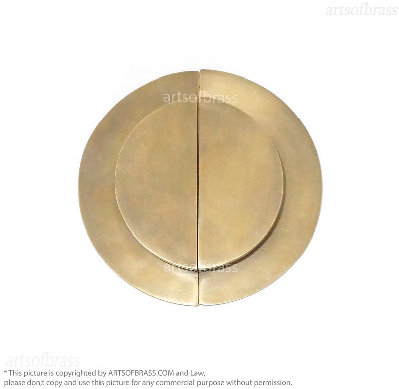 May include: A pair of round, brass door pulls with a concentric circle design. The pulls are separated by a thin vertical line.