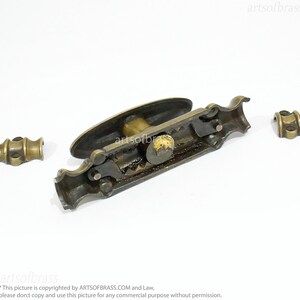May include: Brass window latch with a decorative handle and a mechanism that is visible. The latch is in three pieces, with two separate pieces that attach to the main piece.