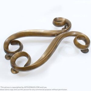May include: A decorative brass door handle with a unique, swirling design. The handle is made of solid brass and has a polished finish.