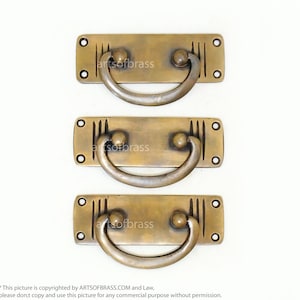 May include: Three antique brass drawer pulls with a rectangular base and a curved handle. The pulls have a decorative design with vertical lines and rounded knobs on each side of the handle.