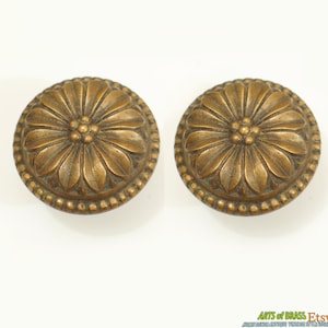May include: Two antique brass door knobs with a floral design. The knobs have a raised, detailed flower pattern with a beaded edge.