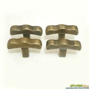May include: Four antique brass cabinet knobs with a wavy top and a T-shaped base.