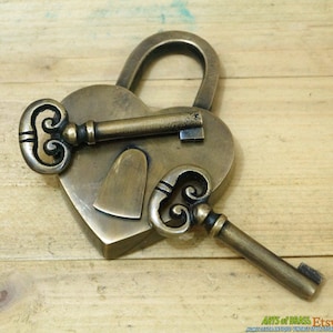 May include: A heart-shaped brass padlock with two ornate keys. The padlock has a keyhole in the shape of a heart. The keys are both made of brass and have intricate designs.