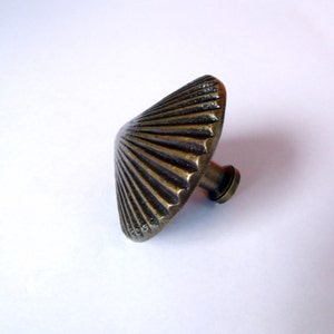 May include: A brass cabinet knob with a fluted, fan-shaped design. The knob has a round base and a short stem.